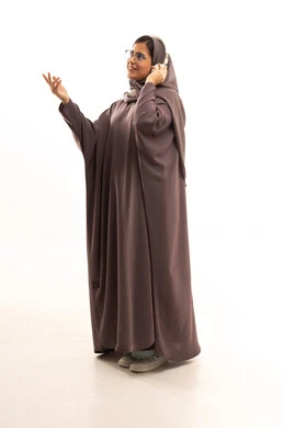 قضاء اوقات ممتعة ومسلية، مفهوم الإصغاء والإستماع، استخدام تقنيات الهيدفون، بورتريه من الجانب لامرأة عربية خليجية سعودية ترتدي الحجاب و العباءة تضع سماعات الرأس الصوتية تستمع إلى الموسيقى ترفع يدها بايماءات الاندماج، صورة لكامل الجسم، خلفية بيضاء