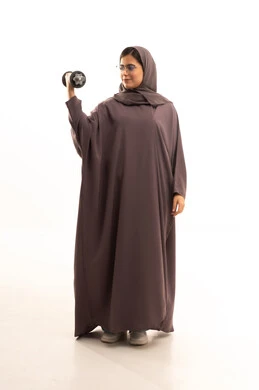 Exercising and lifting weights with dumbbells, a portrait of a smiling Saudi Arabian Gulf woman wearing a hijab and an abaya, looking at the camera while holding heavy weights in her hand, maintaining health and physical fitness, full-body shot, white background.