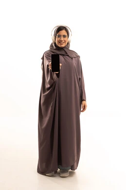A display of a blank black screen on a mobile phone, using advanced modern technology and devices, a portrait of a smiling Saudi Arabian Gulf woman wearing a hijab and an abaya, with headphones, looking at the camera with gestures of joy, full-body, white background.