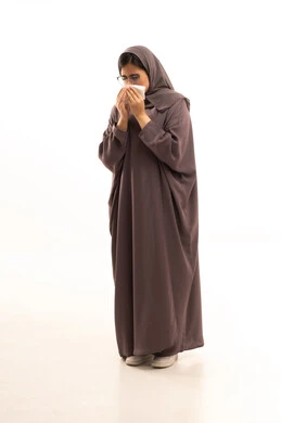 Infection with the coronavirus COVID-19, using paper tissues while sneezing, a portrait of a Saudi Arabian Gulf woman wearing a hijab and an abaya who feels very ill and tired, facial and hand gestures indicating sneezing, full-body, white background.