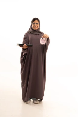 مفهوم تنظيم و إدارة الوقت, الاستعداد للعام الدراسي الجديد, التعليم في المملكة العربية السعودية, بورتريه لطالة عربية خليجية سعودية ترتدي  العباءة و الحجاب تمسك بيدها ساعة المنبة و مجموعة من الكتب, الجسم بالطول الكامل, خلفية بيضاء