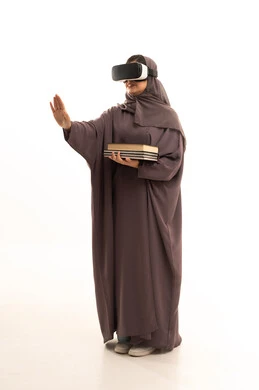 محاكاة العالم الخيالي، دمج التقنيات الحديثة بالتعلم والتدريب، التعليم باستخدام تقنية العالم الافتراضي، بورتريه  لطالبة عربية خليجية سعودية محجبة ترتدي العباءة و الحجاب تضع نظارة الفي ار ثلاثية الأبعاد تحمل مجموعة من الكتب، صورة لكامل الجسم، خلفية بيضاء
