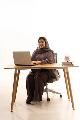 استخدام الأجهزة التقنية الحديثة لمتابعة المحاضرات، المناهج والمواد التعليمية في المملكة، مفهوم التعليم عن بعد، بورتريه  لطالبة جامعية عربية خليجية سعودية محجبة تجلس على الطاولة تقوم باستخدام الحاسب المحمول فى المذاكرة، خلفية بيضاء