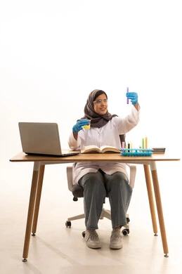 البحث العلمي والتطوير عبر التفاعلات الكيميائية، اكتساب المعرفة والخبرة بإيماءات الدقة والتركيز، الدراسات والتجارب في بيئة عملية متطورة, بورتريه لطالبة عربية خليجية سعودية ترتدي  المعطف الأبيض ونظارات الحماية تمسك بيدها الأنبوب الزجاجي تجلس امام الحاسوب المحمول يقوم بتجربة علمية، خلفية بيضاء