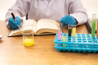 Developing chemical experiments through field scientific research, a close-up portrait of the hand of a Saudi Gulf Arab female student sitting in front of a laptop, taking notes and recording results, with a white background.