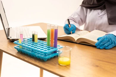 The concept of biochemistry, research and development, conducting chemical experiments for scientific research and developing results, a close-up portrait of the hand of a Gulf Arab Saudi female student sitting in front of a laptop writing down results and notes, white background.