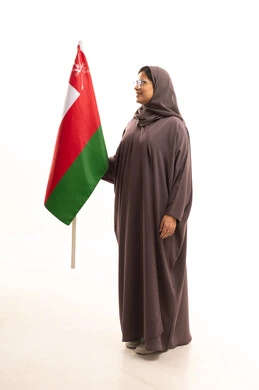 Loyalty to the homeland and pride in belonging to it, commemorating the founding of the state in 1775 AD, cultures and national symbols, a side portrait of an Arab Gulf Omani woman wearing glasses, a hijab, and an abaya holding the national flag of the country celebrating the anniversary of Omani National Day on November 18, full-body, white background.