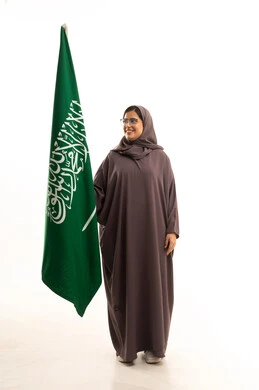 الاعتزاز بالهوية الوطنية والانتماء للبلاد، ذكرى يوم بدينا 1727 م، يوم العلم السعودي11 مارس، الاحتفال بتأسيس الدولة السعودية الأولى 22 فبراير، بورتريه لإمرأة عربية خليجية سعودية ترتدي العباءة و الحجاب و نظارة نظر تمسك راية وشعار المملكة تنظر بتعابير الفخر, الجسم بالطول الكامل, خلفية بيضاء