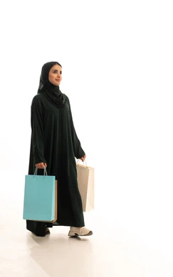 ايماءات المشي و الذهاب إلى مكان معين، تخفيضات وعروضات موسمية في الأسواق، ايماءات السرور بعد التسوق والشراء وتأثيره الإيجابي على المرأة, بورترية لسيدة عربية سعودية خليجية مبتسمة محجبة ترتدي عباءة سوداء تحمل بيدها أكياس تسوق ملونه،  الجسم بالطول الكامل، خلفية بيضاء