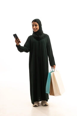 Exploiting major offers, buying necessities and clothes from shopping malls, using modern and advanced devices and technologies, browsing mobile applications to purchase products, a portrait of a Saudi Gulf Arab woman wearing a hijab and abaya holding a mobile phone and shopping bags, full-body, white background.