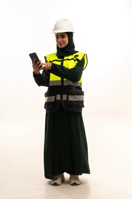 دمج التكنولوجيا المتطورة بالهندسة، العمل في القطاع الهندسي, بورتريه لمهندسة عربية خليجية سعودية ترتدي العباءة  والخوذة وسترة الحماية تقوم بمتابعة سير الأعمال عن بعد عبر الهاتف المحمول، الأجهزة التقنية الحديثة، الجسم بالطول الكامل،خلفية بيضاء