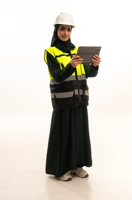 مهن ووظائف سعودية نسائية، تحقيق الثورة الصناعية وكفاءة الإنتاج و التصنيع، اعتماد التقنيات والتكنولوجيا الحديثة في الهندسة, بورترية لمهندسة صناعية عربية سعودية خليجية ترتدي سترة وخوذة الحماية تتابع سير أعمال المصنع بإستخدام جهاز التابلت، الجسم بالطول الكامل، خلفية بيضاء