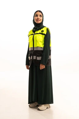 Looking at something, working in the engineering sector, construction by the hands of the nation's sons, monitoring and supervising engineering projects, a portrait of a Saudi Gulf Arab engineer wearing a black abaya with a safety vest standing upright and straight, full-body, white background.