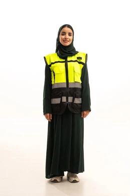 النظر إلى الكاميرا بإيماءات السعادة والسرور، العمل في القطاع الهندسي, الإعمار بسواعد أبناء الوطن, المتابعة والإشراف على المشاريع الهندسية, بورتريه لمهندسة عربية خليجية سعودية  ترتدي العباءة السوداء مع سترة الحماية تقف باستقامة واعتدال, الجسم بالطول الكامل, خلفية بيضاء