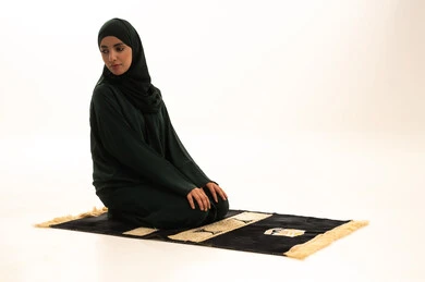 الالتزام بأداء الفروض على وقتها, التقرب الى الله بالإجتهاد في العبادة والحفاظ على الصلوات، بورتريه لإمرأة عربية سعودية خليجية ترتدي الحجاب والعباءة السوداء تجلس على سجادة الصلاة تقوم بالتسليم، خلفية بيضاء