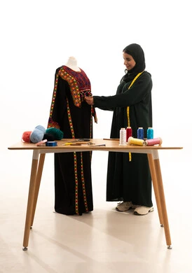 اعمال وحرف يدوية، بورتريه لامراة عربية خليجية سعودية ترتدي الحجاب و العباءة السوداء تعمل على أخذ القياسات، مصممة أزياء مبتكرة، ورشة عمل تصميم ازياء، أدوات الخياطة، مهن وأعمال فن الخياطة، فنون ومهارات تصميم وتفصيل الملابس النسائية ، مفهوم عالم الأزياء والموضة، خلفية بيضاء