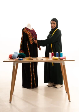 Looking at the camera with expressions of happiness, a portrait of a Gulf Arab Saudi woman wearing a hijab and a black abaya taking measurements, an innovative fashion designer, a fashion design workshop, sewing tools, professions and crafts of the art of sewing, arts and skills of designing and tailoring women's clothing, the concept of the world of fashion and style, white background.