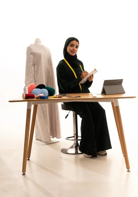 مفهوم إدارة المشاريع عن بعد, بورتريه لإمرأة عربية خليجية سعودية محجبة ترتدي عباءة سوداء تجلس على الطاولة الخشبية تقوم بانجاز مهام العمل عبر جهاز التابلت ، تدوين و تسجيل الملاحظات, إستخدام اجهزة تقنية حديثة للعمل، التسوق الإلكتروني الآمن،  مفهوم عالم الأزياء والموضة، خلفية بيضاء