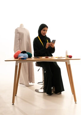Chatting with family and friends, browsing social media apps and websites, the concept of the world of fashion and style, a portrait of an Arab Gulf Saudi fashion designer wearing a black abaya and hijab holding a mobile phone in her hand, white background.