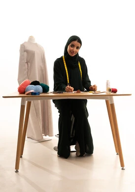 تنظيم وإدارة الأعمال, تدوين وتسجيل المعلومات على الورق، فنون ومهارات تصميم الملابس النسائية، بورتريه لمصممة عربية خليجية سعودية ترتدي الحجاب والعباءة تمسك بيدها قلم تقوم بالكتابة على نوت تنظر الى الكاميرا بايماءات السعادة و السرور، مفهوم عالم الأزياء والموضة، خلفية بيضاء