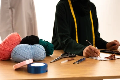 تدوين المهام اليومية، فنون ومهارات تصميم الملابس النسائية، بورتريه مقرب لمصممة عربية خليجية سعودية ترتدي الحجاب والعباءة تمسك بيدها قلم تقوم بالكتابة على نوت، مفهوم عالم الأزياء والموضة، خلفية بيضاء