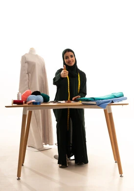 Looking at the camera with expressions of joy, the arts and skills of women's clothing design, a portrait of a Gulf Arab Saudi designer wearing a hijab and abaya, raising her thumb up with gestures of approval and agreement, the concept of the fashion and style world, full-body, white background.