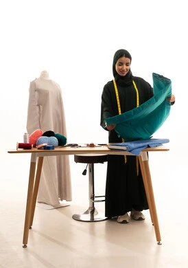 تفصيل الثياب العصرية بجودة عالية، فنون ومهارات تصميم الملابس النسائية، بورتريه لمصممة عربية خليجية سعودية ترتدي الحجاب والعباءة تمسك بيدها القماش تنظر بإيماءات السعادة و السرور، مفهوم عالم الأزياء والموضة، الجسم بالطول الكامل، خلفية بيضاء