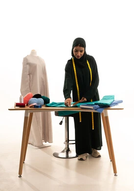 تفصيل الملابس النسائية ، مهن و أعمال الخياطة و التصميم , بورتريه لمصممة أزياء عربية خليجية سعودية ترتدي العباءة السوداء والحجاب تأخذ القياسات بالمسطرة الخشبية، الجسم بالطول الكامل، خلفية بيضاء