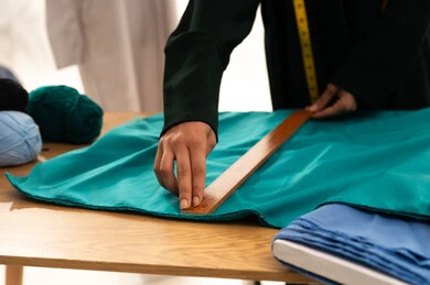Professions and works of sewing and design, tailoring women's clothing, a close-up portrait of the hand of an Arab Gulf Saudi fashion designer wearing a black abaya taking measurements with a wooden ruler, white background.