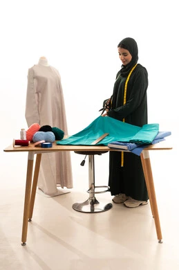 بورترية لشابة عربيه سعودية خليجية تمسك بيديها المقص تقوم بقص القماش ، استخدام الأدوات المناسبة لتفصيل طقم خاص لاحدى الزبائن ، محل خياطة و تفصيل الملابس  النسائية في السعودية ، مهارة الخياطة واتقان تفصيل الملابس الشبابية
