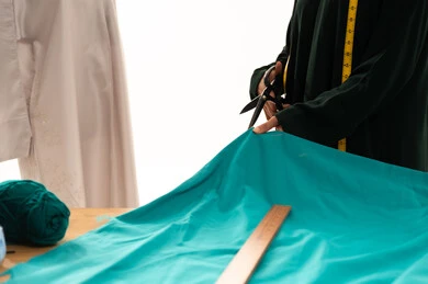 A sewing and tailoring shop for women's clothing in Saudi Arabia, a close portrait of a young Arab Saudi Gulf woman wearing a black abaya holding scissors in her hands, cutting fabric, using the appropriate tools to tailor a special outfit for one of the customers, sewing skills and mastery of tailoring youth clothing. A sewing and tailoring shop for women's clothing in Saudi Arabia, a close portrait of a young Arab Saudi Gulf woman wearing a black abaya holding scissors in her hands, cutting fabric, using the appropriate tools to tailor a special outfit for one of the customers, sewing skills and mastery of tailoring youth clothing.