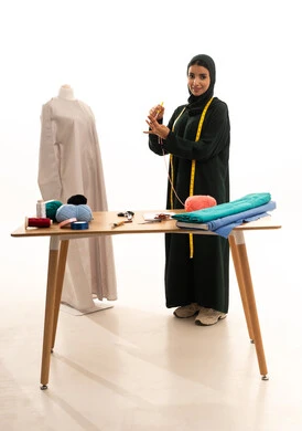 Skill of clothing design, crafts and manual professions in Saudi Arabia, a portrait of an Arab Gulf Saudi fashion designer wearing an abaya and hijab, sewing clothes using a needle and wool thread, full-body, white background. Skill of clothing design, crafts and manual professions in Saudi Arabia, a portrait of an Arab Gulf Saudi fashion designer wearing an abaya and hijab, sewing clothes using a needle and wool thread, full-body, white background.