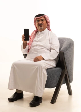 اشاشة سوداء على جهاز محمول، تصفح مواقع التواصل الاجتماعي على المحمول، استخدام التقنيات الحديثة في العمل عن بعد، بورتريه مقرب لرجل كبير السن عربي خليجي سعودي يرتدي الزي التقليدي والشماغ يمسك الهاتف المحمول، إنجاز المهام اونلاين من خلال التكنولوجيا، خلفية بيضاء .