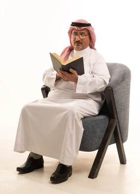 Reading with gestures of contemplation and focus, acquiring knowledge and information, spending free time on education and learning, the concept of literacy, a close-up portrait of an elderly Arab Saudi Gulf man wearing a ghutrah and traditional thobe practicing the hobby of reading useful books in his free time, white background.