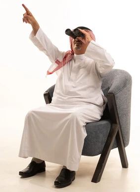 الاشارة إلى شيء ما، رؤى مستقبلية عند الراشدين والكبار بالسن، حب الاستكشاف والمغامرة، بورتريه لرجل كبير مسن عربي سعودي خليجي مبتسم يرتدي الثوب التقليدي والشماغ يقوم بالنظر من خلال المنظار ثنائي العينين(التلسكوب)، رؤية الأشياء البعيدة بالتلكسوب، خلفية بيضاء.