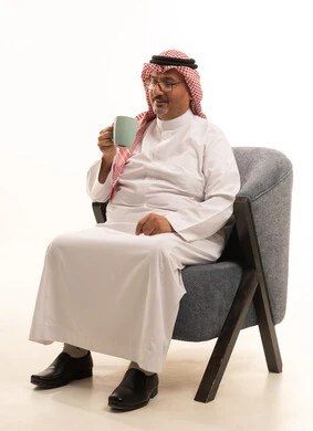 تناول المشروبات والأعشاب الساخنة في الشتاء، حسن الضيافة والاستقبال، شرب القهوة لتحسين المزاج، بورتريه لرجل كبير مسن عربي سعودي خليجي يرتدي الثوب التقليدي والشماغ يمسك بيده كوب باللون الرمادي، قضاء أوقات ممتعة في وقت الفراخ، خلفية بيضاء.