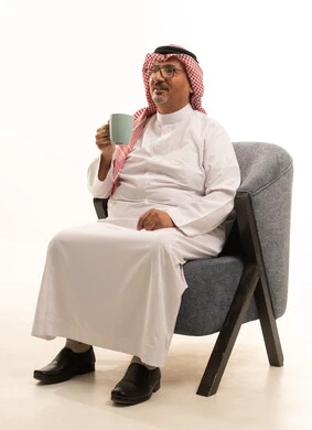 شرب القهوة لتحسين المزاج، تناول المشروبات والأعشاب الساخنة في الشتاء، حسن الضيافة والاستقبال، بورتريه لرجل كبير مسن عربي سعودي خليجي يرتدي الثوب التقليدي والشماغ يمسك بيده كوب باللون الرمادي، قضاء أوقات ممتعة في وقت الفراخ، خلفية بيضاء.