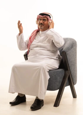 قضاء أوقات ممتعة ومسلية، الإصغاء والاستمتاع باستخدام الهيدفون، الاستماع إلى المواهب الغنائية الفنية، بورتريه لرجل عربي خليجي سعودي كبير بالسن يرتدي الثوب التقليدي والشماغ يضع سماعة الرأس ويستمتع بسماع اغاني منوعة، خلفية بيضاء