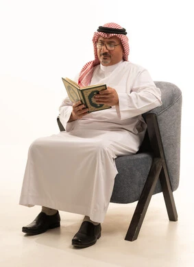 الشعور بالخشوع والطمأنينه, تلاوة وقراءة القرآن الكريم، بورتريه لرجل عربي سعودي خليجي يرتدي الشماغ والثوب التقليدي ونظارة طبية يجلس على كرسي مريح يحمل بيده المصحف الشريف, الإكثار من ذكر الله تعالى والإجتهاد في العباده, التقرب الى الله في شهر رمضان, خلفية بيضاء