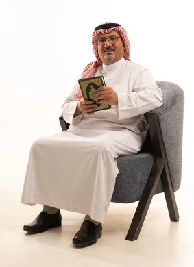 Recitation and reading of the Holy Quran, feeling of humility and tranquility, a portrait of an Arab Saudi Gulf man wearing a ghutrah and traditional thobe with glasses sitting on a comfortable chair holding the Holy Quran in his hand, increasing the remembrance of Allah Almighty and striving in worship, getting closer to Allah during the month of Ramadan, white background.