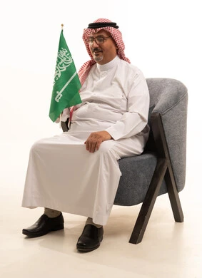 الاعياد والمناسبات الوطنية، الاحتفال بالعيد الوطني السعودي، التقدم بالعمر والهيبة، بورتريه لرجل كبير بالسن عربي خليجي سعودي يرتدي الثوب التقليدي و الشماغ يجلس على كرسي مريح ويمسك علم المملكة, الاهتمام المظهر الخارجي، مفهوم الرجولة العربية, خلفية بيضاء