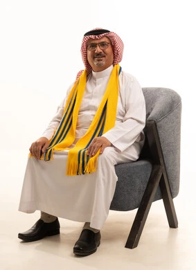 Looking at the camera with gestures of confidence and joy, enthusiasm and interaction with the national team, victory and winning, a portrait of an elderly Arab Gulf Saudi man wearing a ghutrah and traditional thobe sitting on a comfortable chair with a scarf, cheering for his favorite team, different sports clubs, white background.