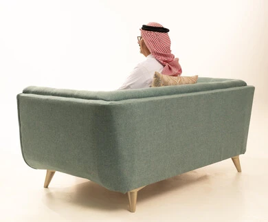 The concept of masculinity and dignity, gestures of self-confidence, attention to external appearance, a portrait from behind of an elderly Arab Gulf Saudi man wearing traditional attire and a ghutrah sitting on a comfortable sofa looking somewhere with expressions of joy, white background.