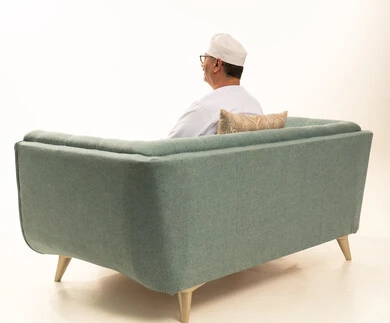 الاهتمام بالمظهر الخارجي، مفهوم الرجولة والوقار، ايماءت الثقة بالنفس، بورتريه من الخلف لرجل عربي خليجي عماني كبير مسن يرتدي الدشداشة والعمامة يجلس على أريكة مريحة ينظر الى مكان ما بتعابيرالسرور، خلفية بيضاء