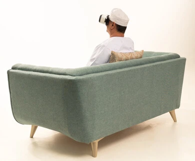 Spending enjoyable and entertaining times with virtual games, enjoying watching virtual reality movies, a portrait from behind of an elderly Arab Gulf Omani man wearing a traditional dishdasha and kumma sitting on a comfortable chair and wearing 3D virtual reality glasses, white background.