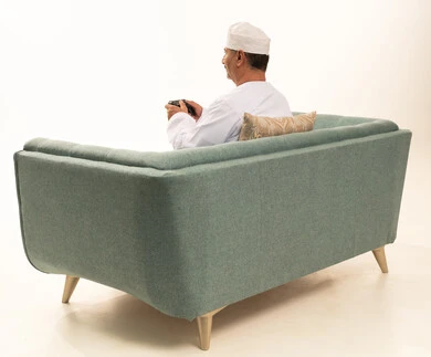 استخدام التكنولوجيا الحديثة في الترفيه، انشطة ترفيهية منزلية، ايماءات الفوز والحماس، قضاء وقت ممتع في المنزل، بورتريه من الخلف لرجل مسن عربي خليجي عماني يرتدي الدشداشة والكمة يجلس على الأريكه يمسك بيده عصا التحكم ، المتعة والتسلية والتفاعل، خلفية بيضاء