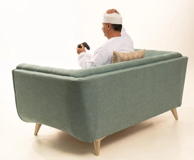 تعابير الحزن والخسارة، قضاء وقت ممتع في المنزل، انشطة ترفيهية منزلية، استخدام التكنولوجيا الحديثة في الترفيه، بورتريه من الخلف لرجل مسن عربي خليجي عماني يرتدي الدشداشة والكمة يجلس على الأريكه يمسك بيده عصا التحكم ، المتعة والتسلية والتفاعل، خلفية بيضاء