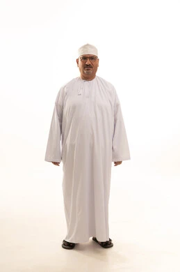 The concept of masculinity and dignity, attention to appearance, a portrait of an elderly Arab Gulf Omani man wearing the traditional dishdasha and Omani kumma, with glasses, standing upright and looking at the camera with gestures of cheerfulness and joy, full-body, white background.