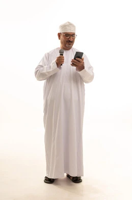 مفهوم الرجولة والوقار، مهارة وفن الألقاء،مهارة وفن الألقاء، تقديم فقرات ثقافية، بورتريه لرجل كبير بالسن عربي خليجي عماني يرتدي الدشداشة التقليدية والكمه العمانية والنظارة الطبية يقف ويحمل مايكروفون وهاتف بإيماءات البشاشة والسرر، الجسم بالطول الكامل، خلفية بيضاء
