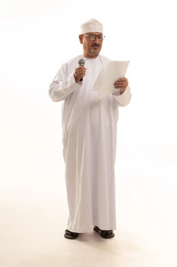 تسجيل المقاطع الصوتية والغنائية، الدورات التدريبية و ورشات العمل، تبادل الحوار والاستفادة من خبرات كبار السن، بورتريه لرجل عربي خليجي عماني يرتدي الدشداشة والعمامة يقف يحمل بيده مكبر الصوت وورقة بيضاء، صورة الجسم بالطول الكامل، خلفية بيضاء